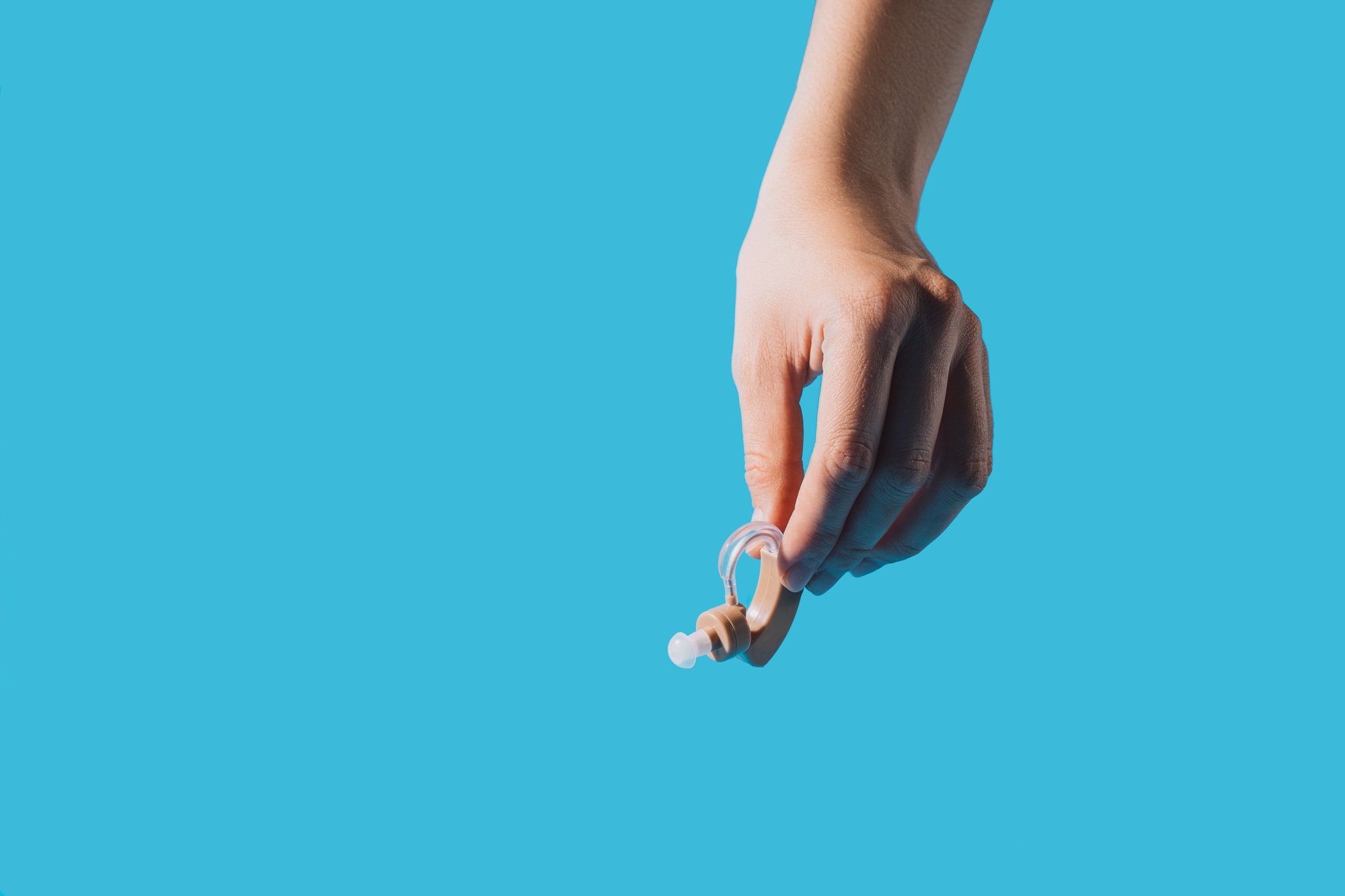 Hearing aid in hand against blue background