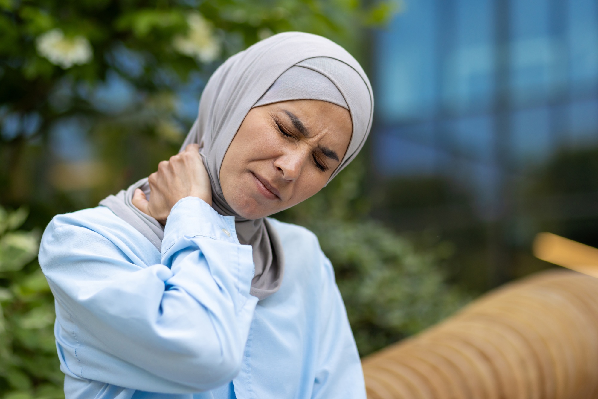 Portrait of unhealthy arabic lady bending head with closed eyes while rubbing neck on blurred