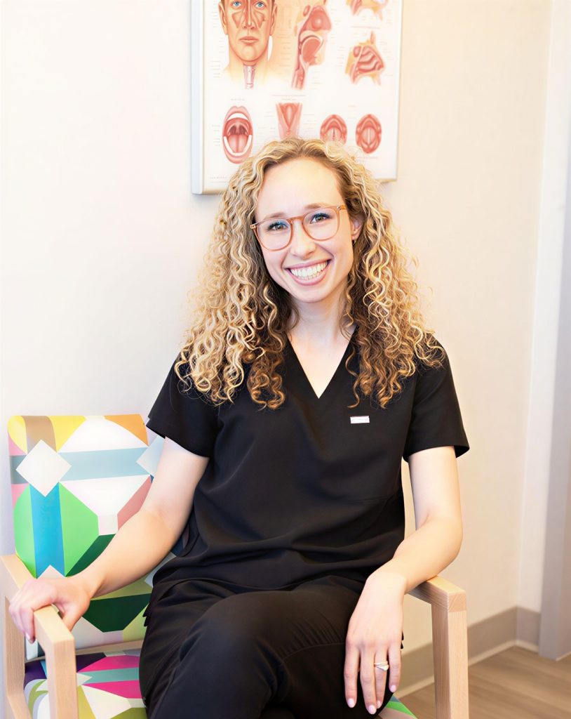 A woman sitting in a chair hands resting on her knees looking thoughtfully ahead