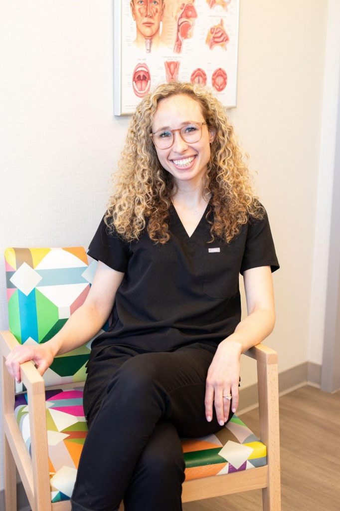 A woman sitting in a chair hands resting on her knees looking thoughtfully ahead