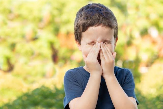 A young boy covering his eyes with his hands expressing surprise or playfulness