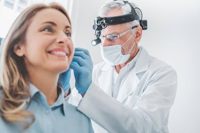 A woman sits in a dental chair while a dentist examines her teeth with a dental tool