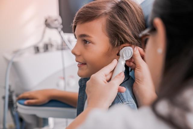 A doctor examines a child's ears with an otoscope during a routine check-up