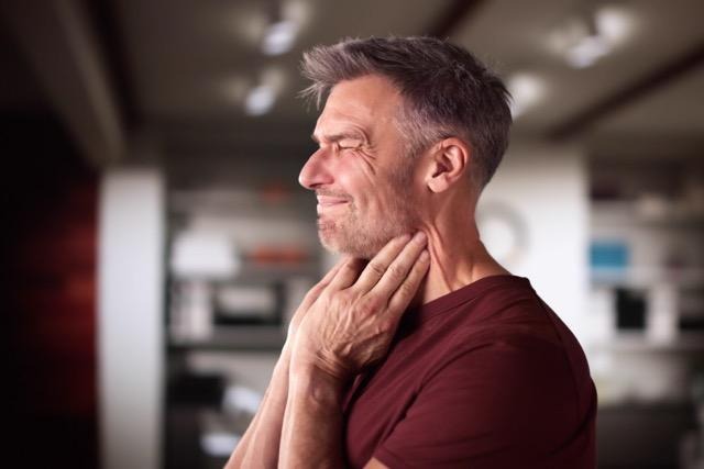 A man grimaces while holding his neck indicating he is experiencing pain