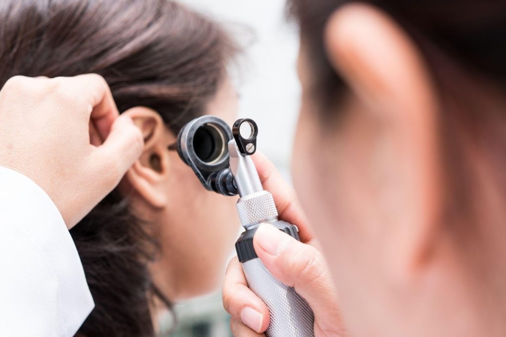A woman uses a stethoscope to examine a person's ear in a clinical setting