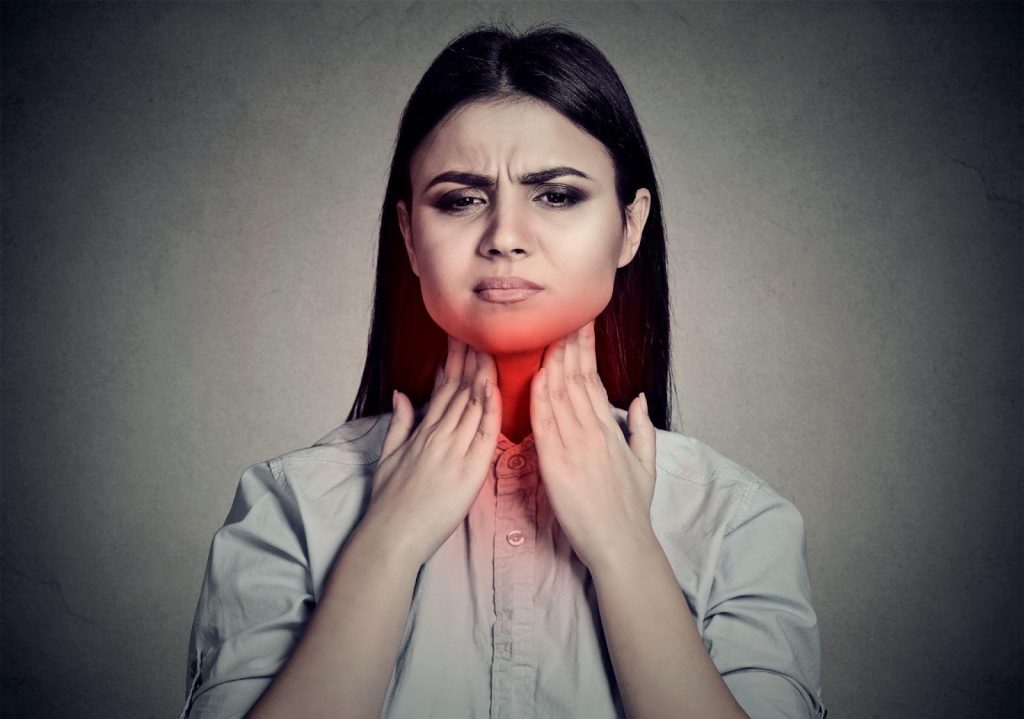 A woman holding her throat showing signs of discomfort from a sore throat