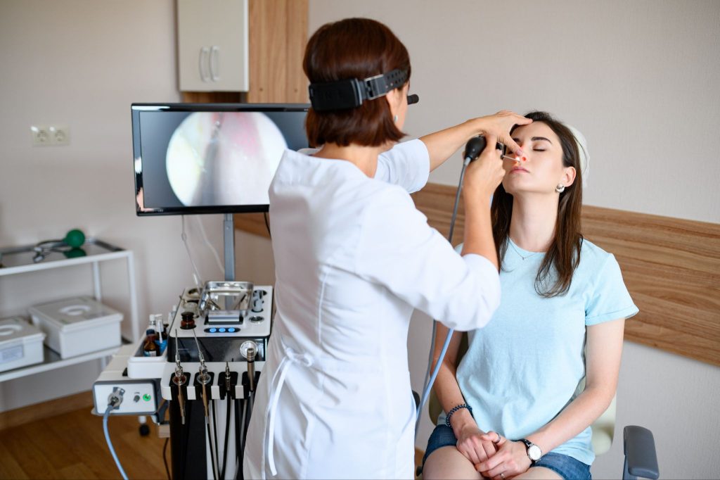 A female ENT specialist performing a nasal endoscopy on a patient using professional medical equipment and a video monitor.