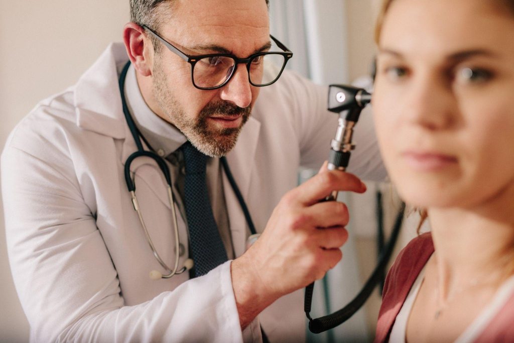 A physician inspects a woman ear with a stethoscope in a clinical setting