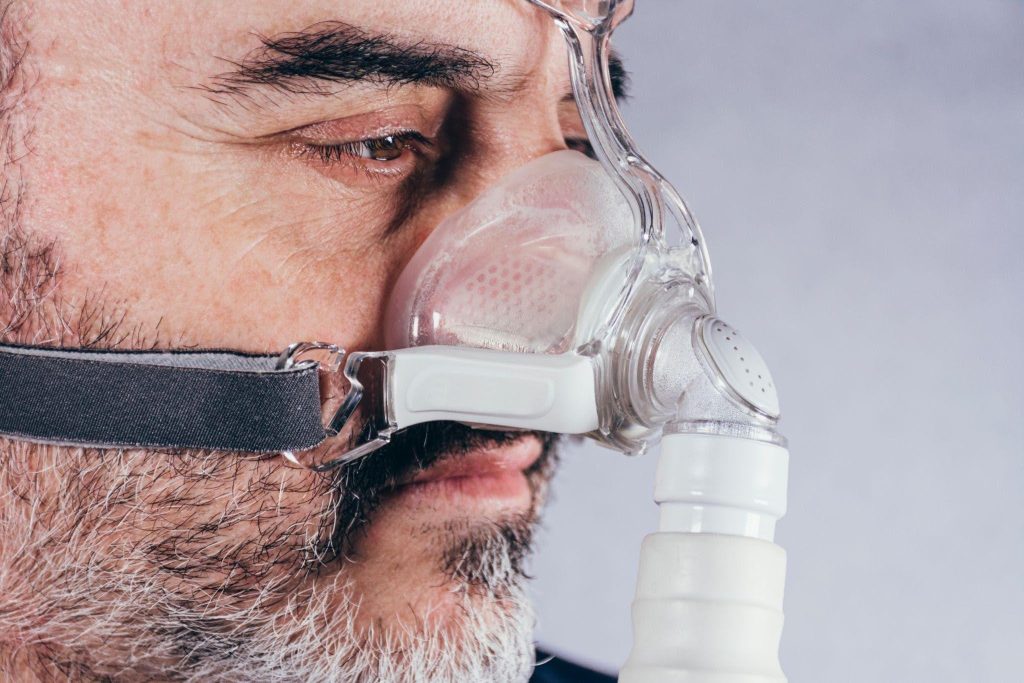 A man with an oxygen mask and breathing device indicating respiratory support in a medical setting