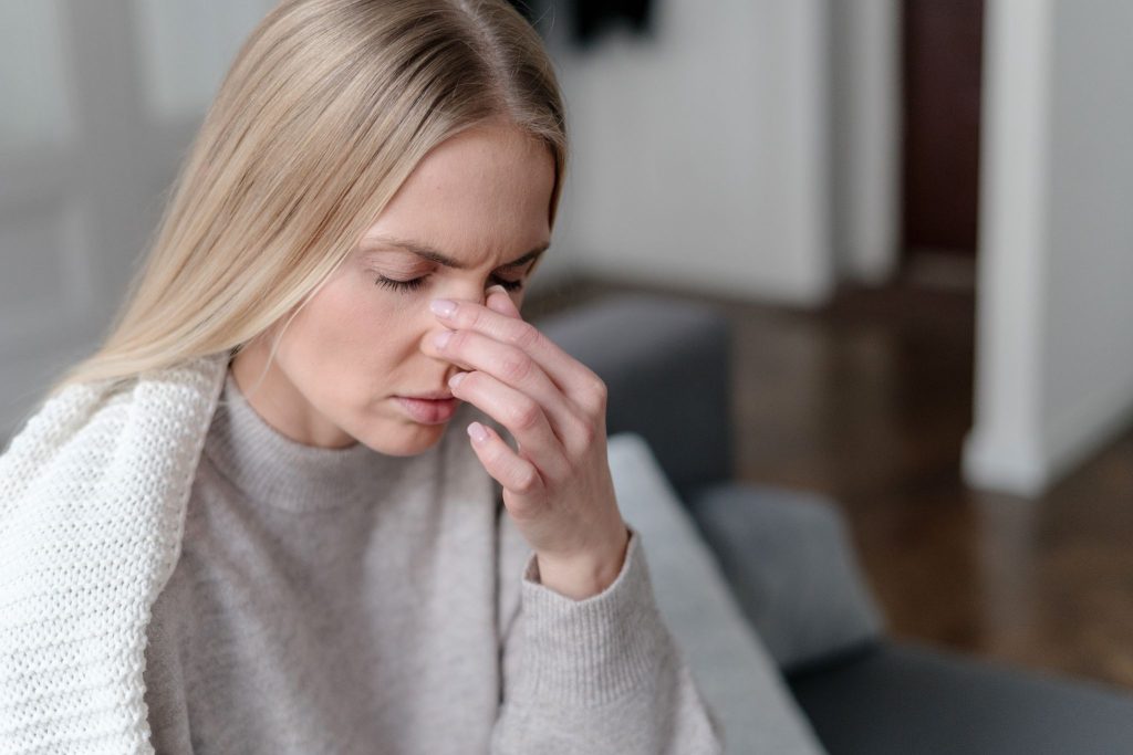 Blonde woman pinching the bridge of her nose while experiencing sinus pain or a headache.