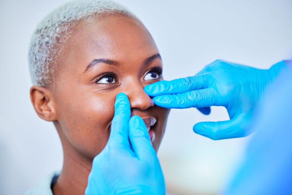 Doctor in blue gloves examining a patient's nose before facial cosmetic surgery.