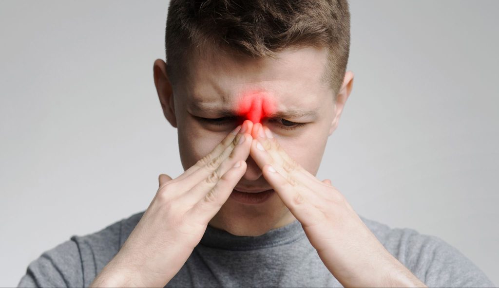 Man pinching the bridge of his nose with highlighted red sinus pain or headache.