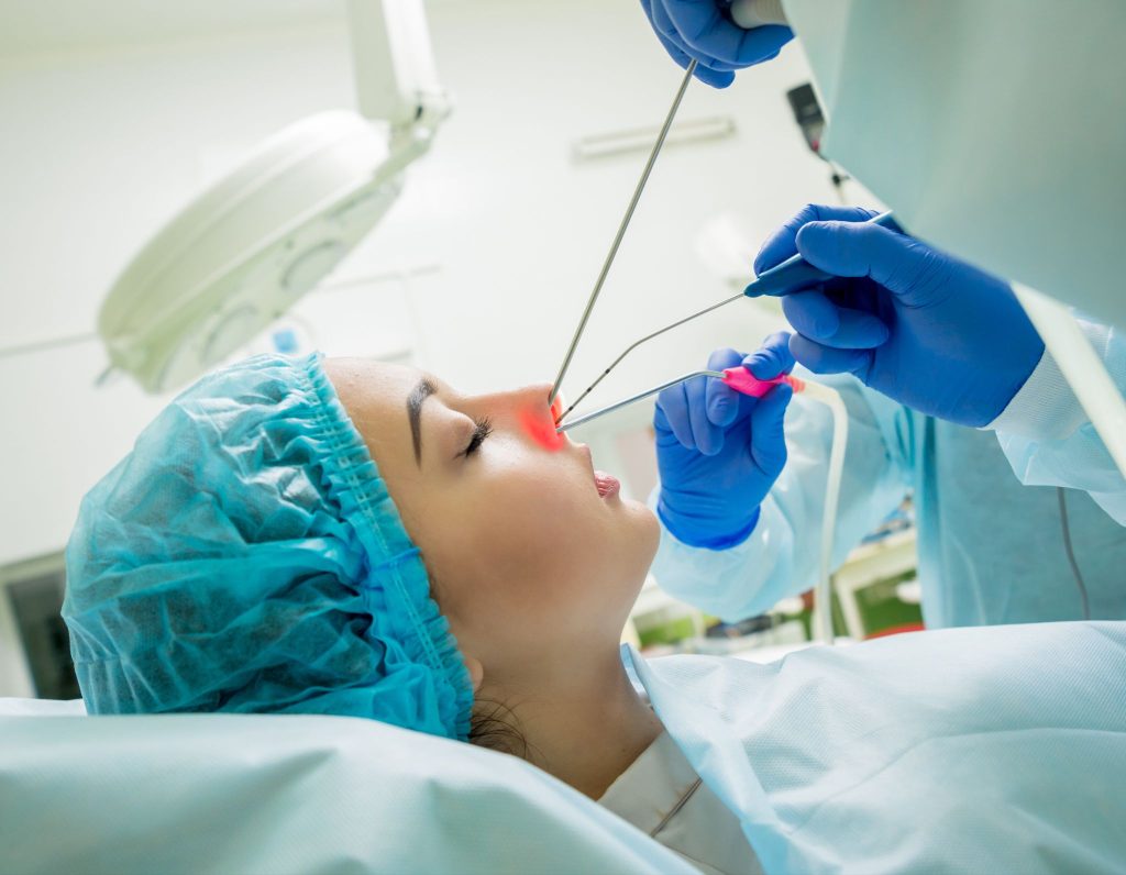Patient wearing a surgical cap undergoing endoscopic laser nasal surgery by a healthcare professional.
