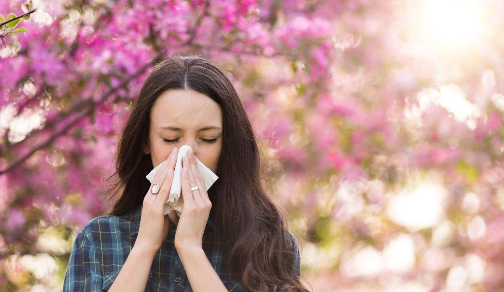 A woman using a tissue to blow her nose positioned in front of a tree highlighting a moment in nature